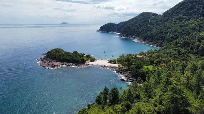 Península de Calhetas vista de drone, com a faixa de areia ligando a ponta de pedra à mata e barcos ancorados
