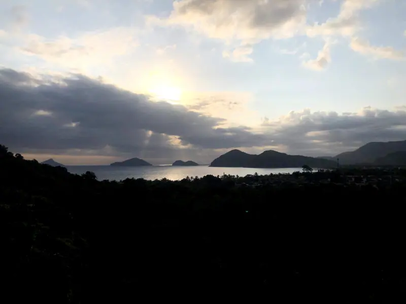 Raios de sol entre as nuvens sobre Camburi e a Praia da Baleia, vistos do alto da mata no fim da tarde