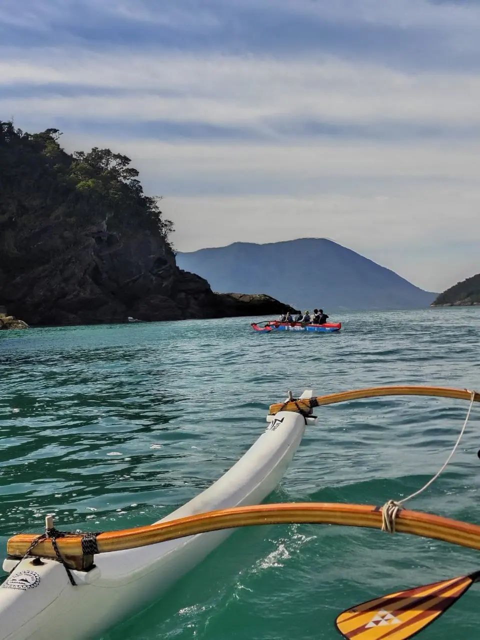 Flutuador lateral e braços da canoa havaiana, com costão e ilha ao fundo
