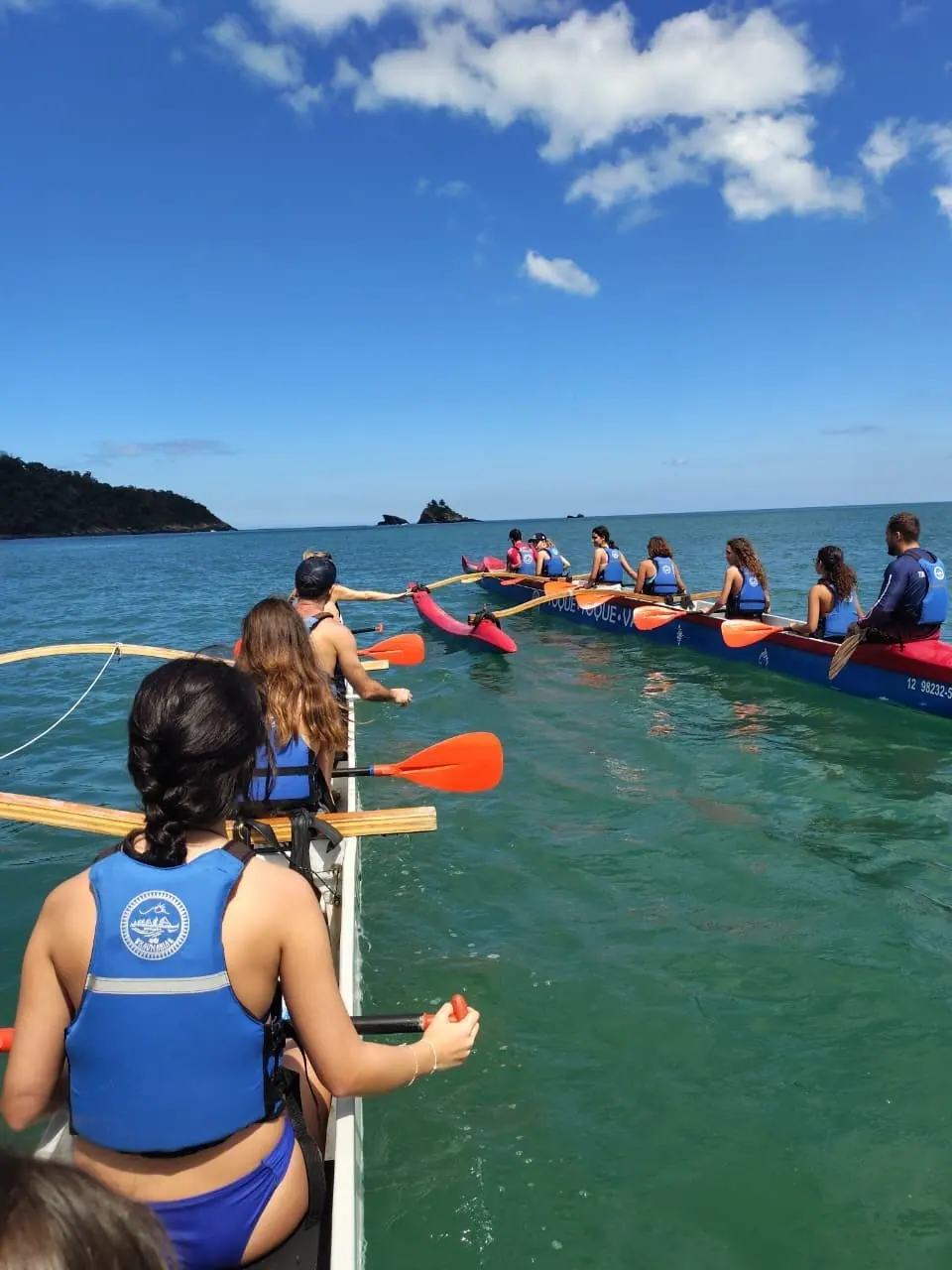 Duas canoas havaianas remando lado a lado no mar verde da Costa Sul