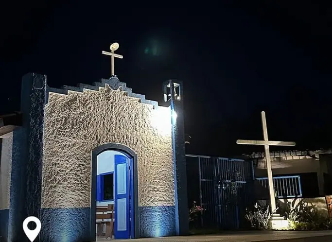 Capela iluminada à noite, com a cruz em frente