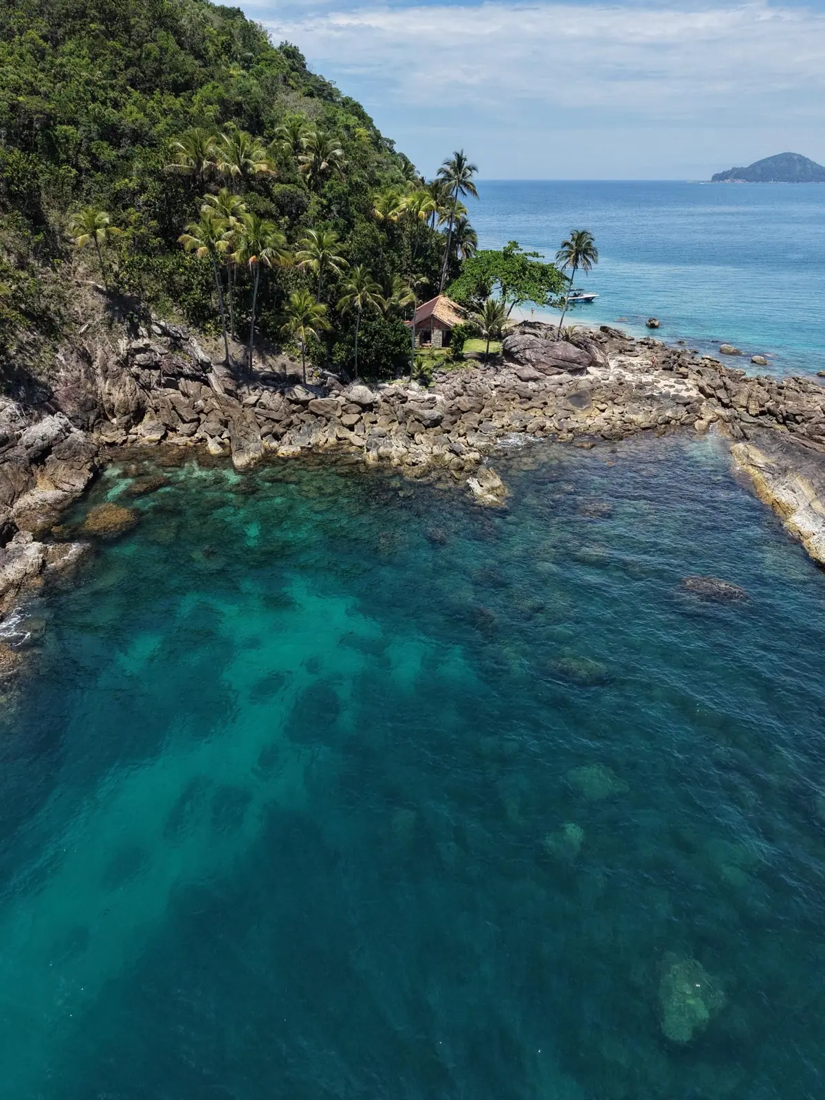 Costão de pedra e água cristalina de uma ilha vistos do alto