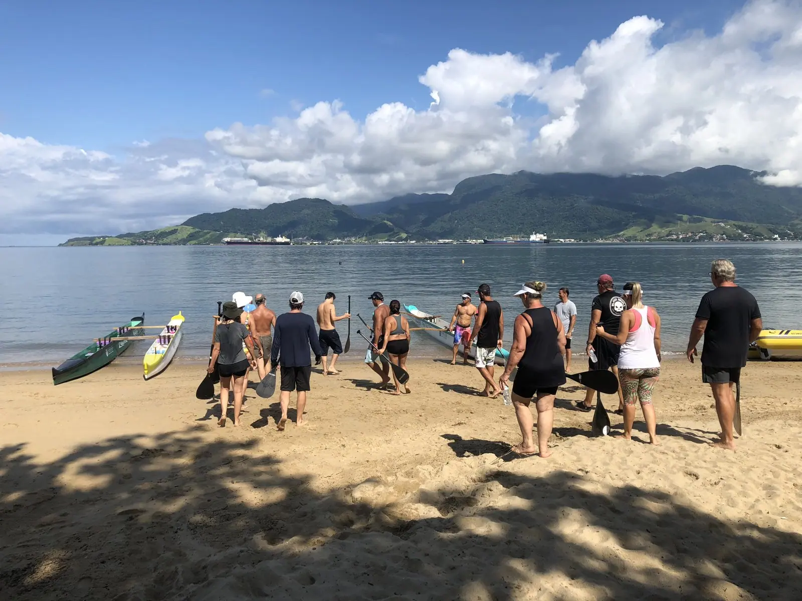 Grupo de remada reunido na areia em Ilhabela, com o canal e a serra ao fundo