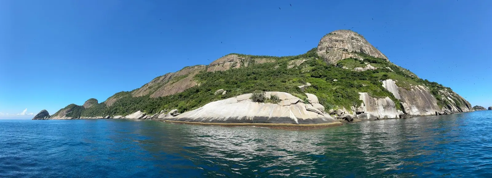 Ilha de mata e pedra no horizonte, vista do mar