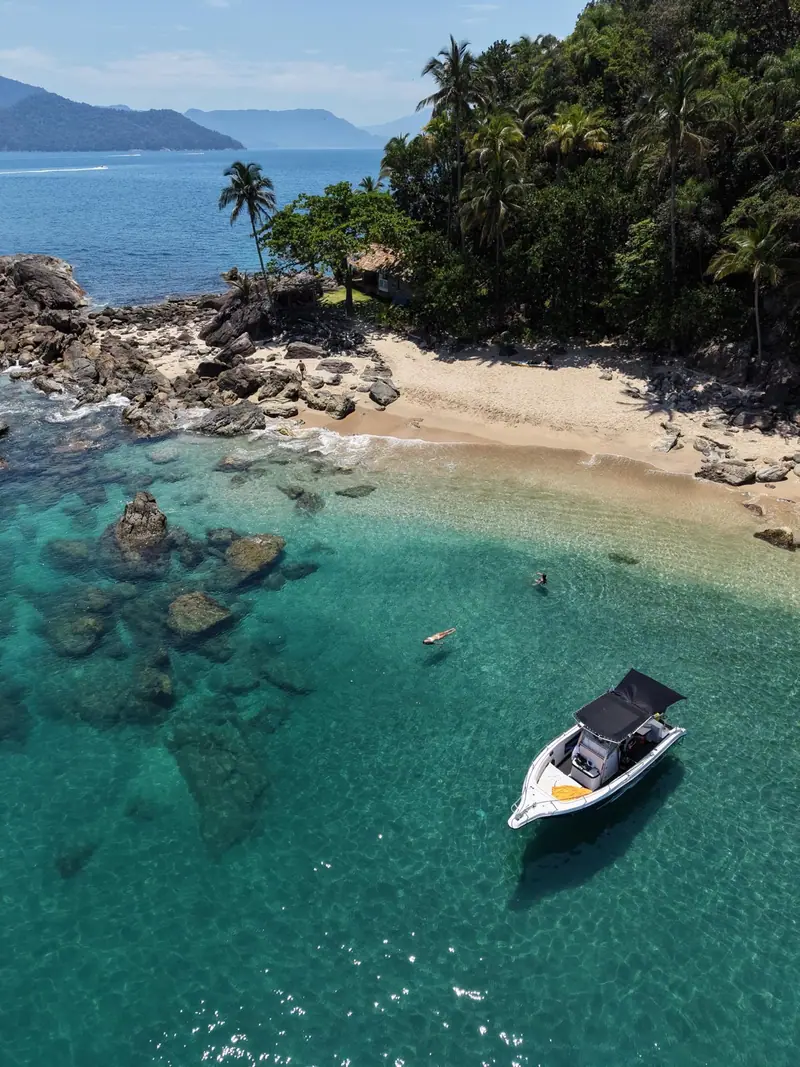 Lancha ancorada diante de uma praia de ilha com coqueiros