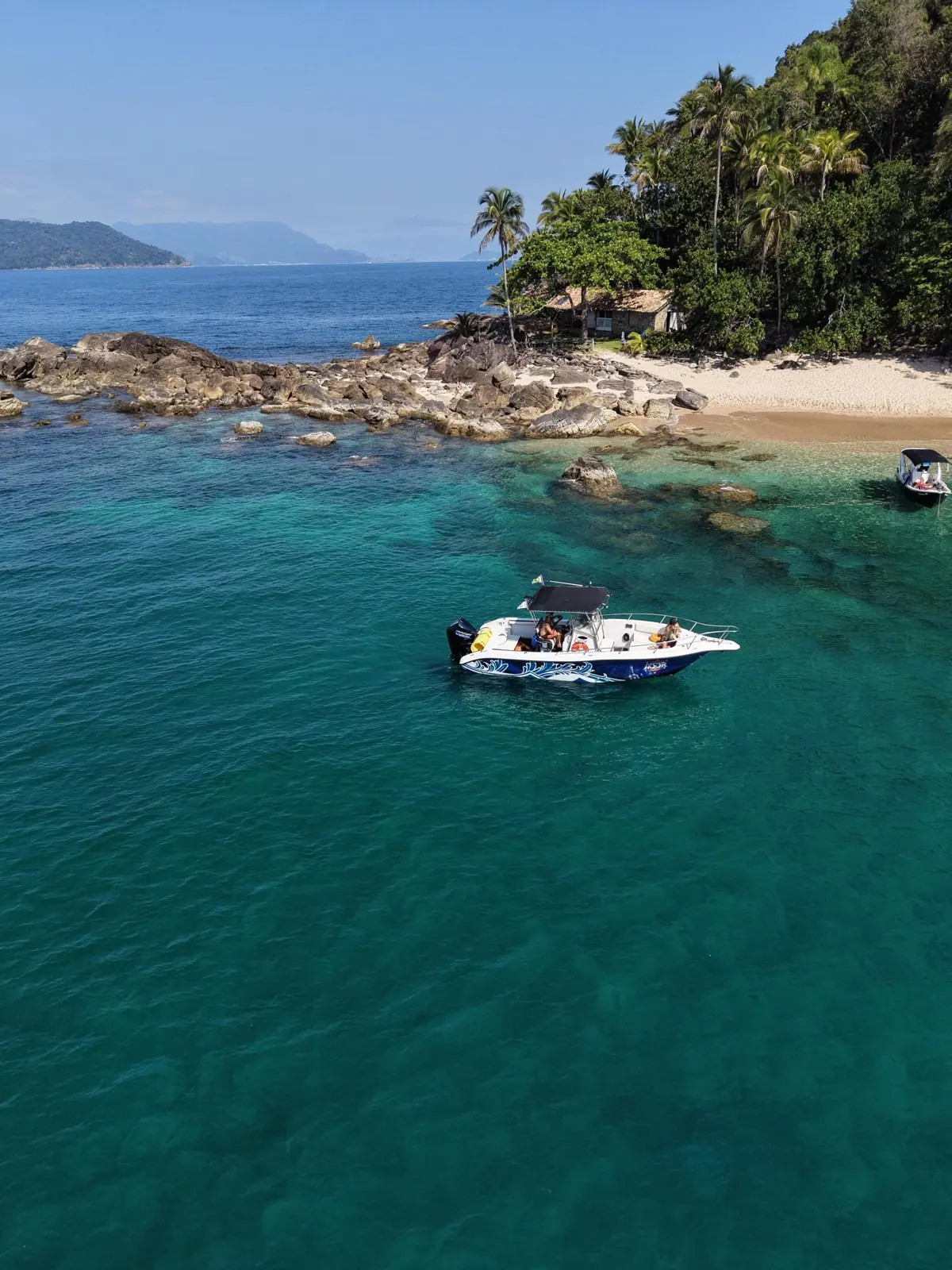 Lancha em enseada de água verde ao lado de uma prainha de ilha