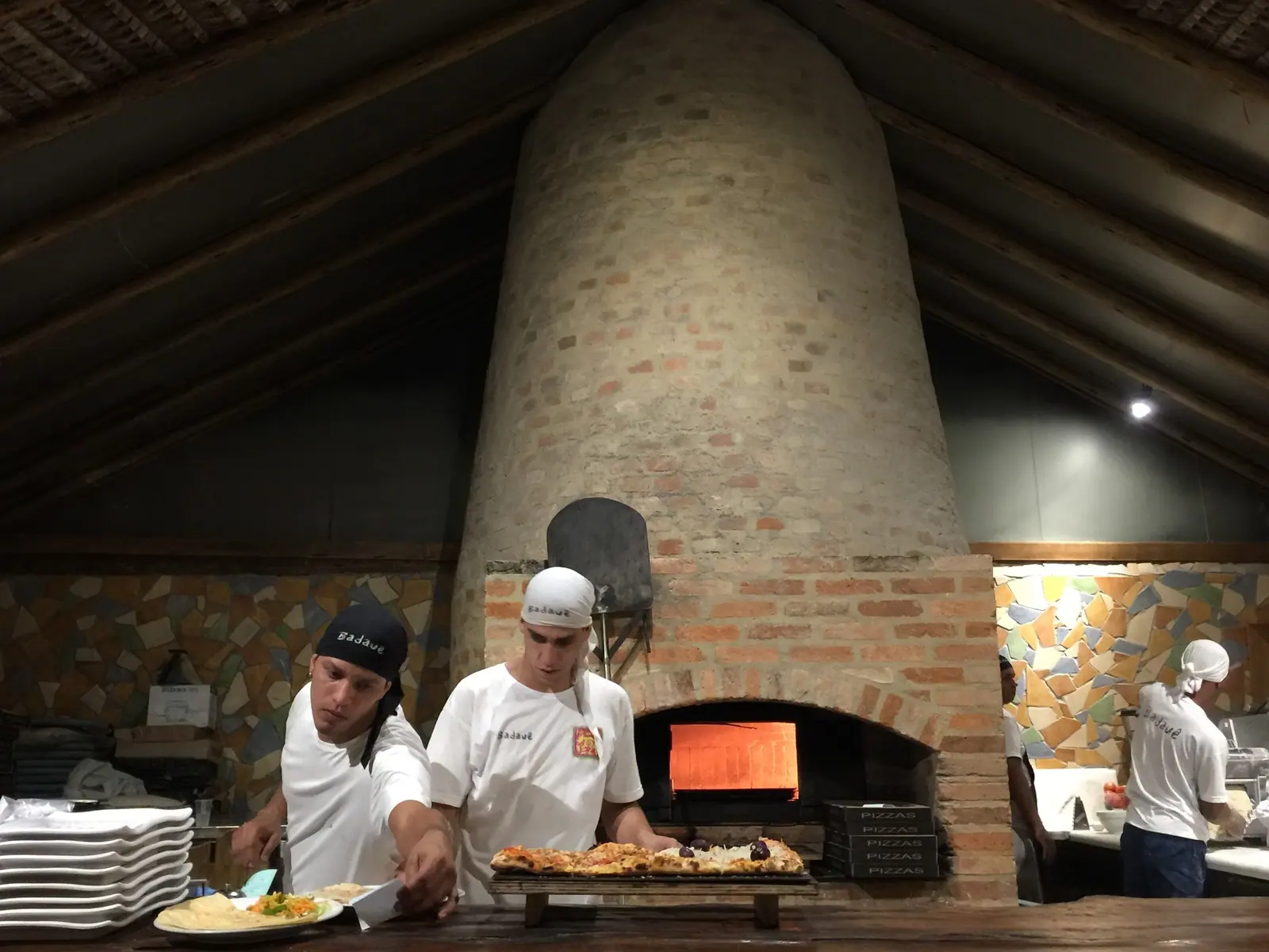 Pizzaiolos trabalhando diante do forno a lenha em restaurante de Maresias