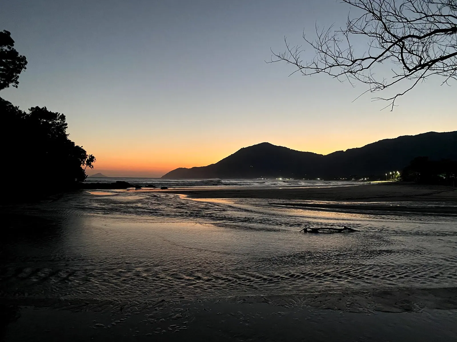 Praia de Maresias ao anoitecer, com o céu alaranjado atrás das montanhas
