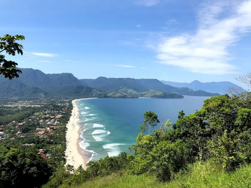 Praia de Maresias vista do alto do mirante, com a faixa longa de areia, as ondas e a Serra do Mar ao fundo
