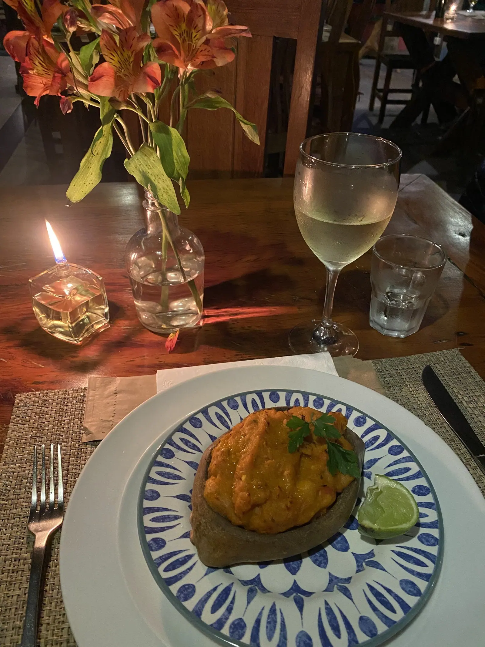 Mesa do restaurante Pimenta de Cheiro à luz de vela, com flores, vinho branco e entrada servida em prato de cerâmica