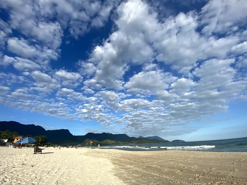 Areia clara da Praia de Santiago sob céu azul com nuvens, com a serra ao fundo