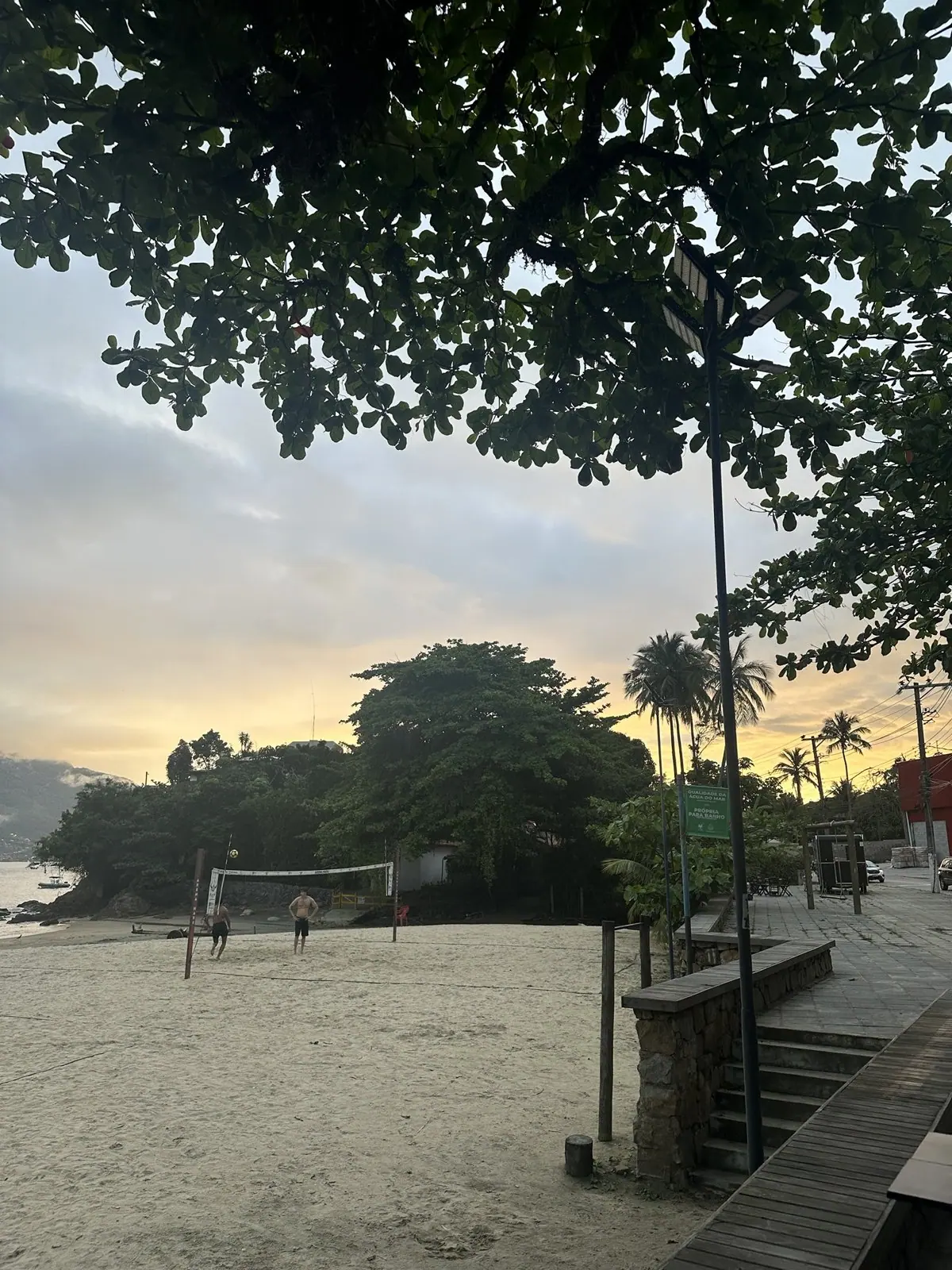 Calçadão e amendoeiras da Praia Preta, em São Sebastião, ao entardecer, com moradores jogando futevôlei