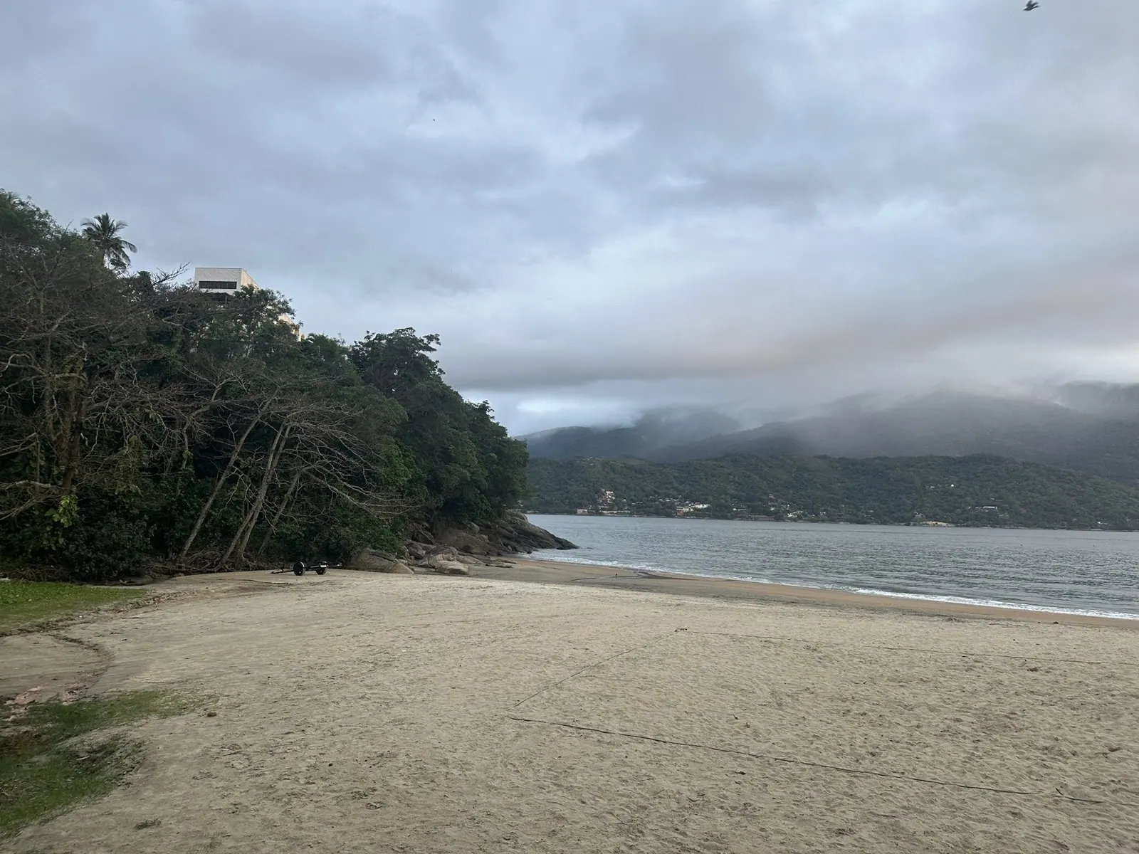 Canto da Praia Preta, em São Sebastião, com costão de pedra, Mata Atlântica e a areia escura perto da água