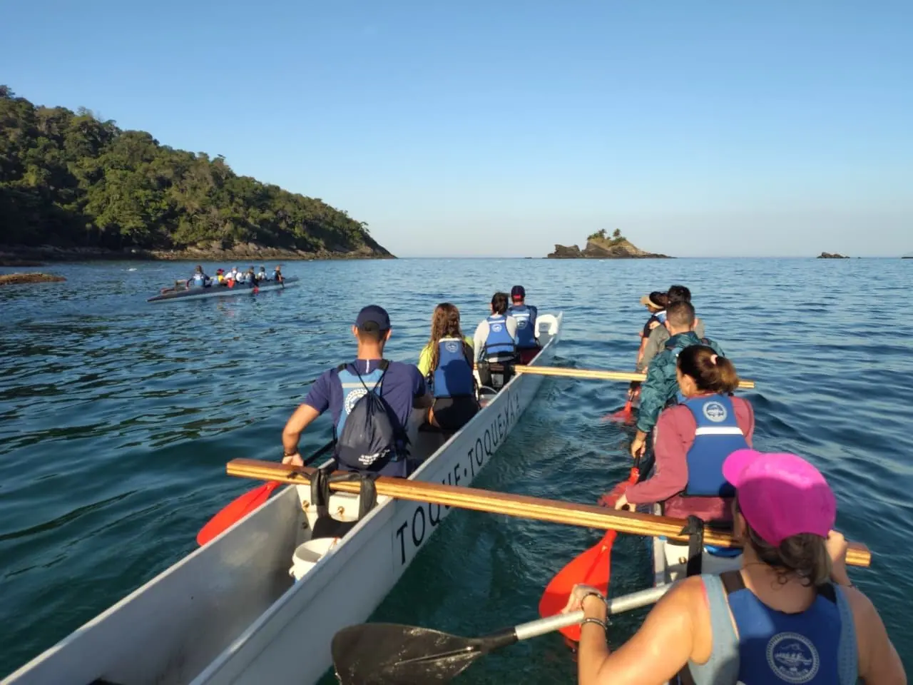 Remada em grupo na canoa havaiana, com ilha ao fundo