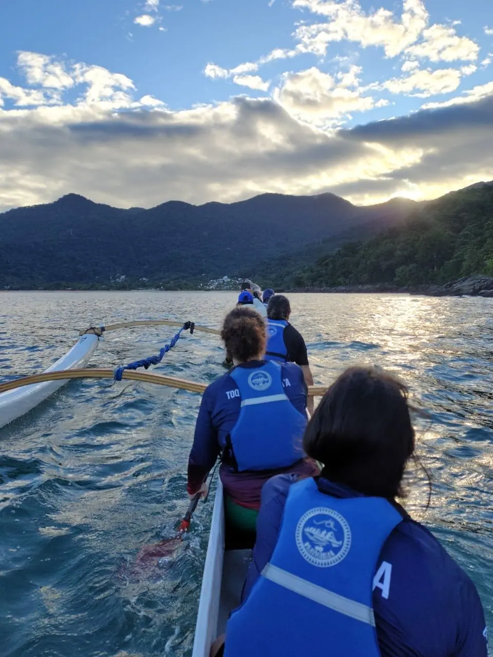 Remadora na canoa havaiana com o sol nascendo atrás das montanhas