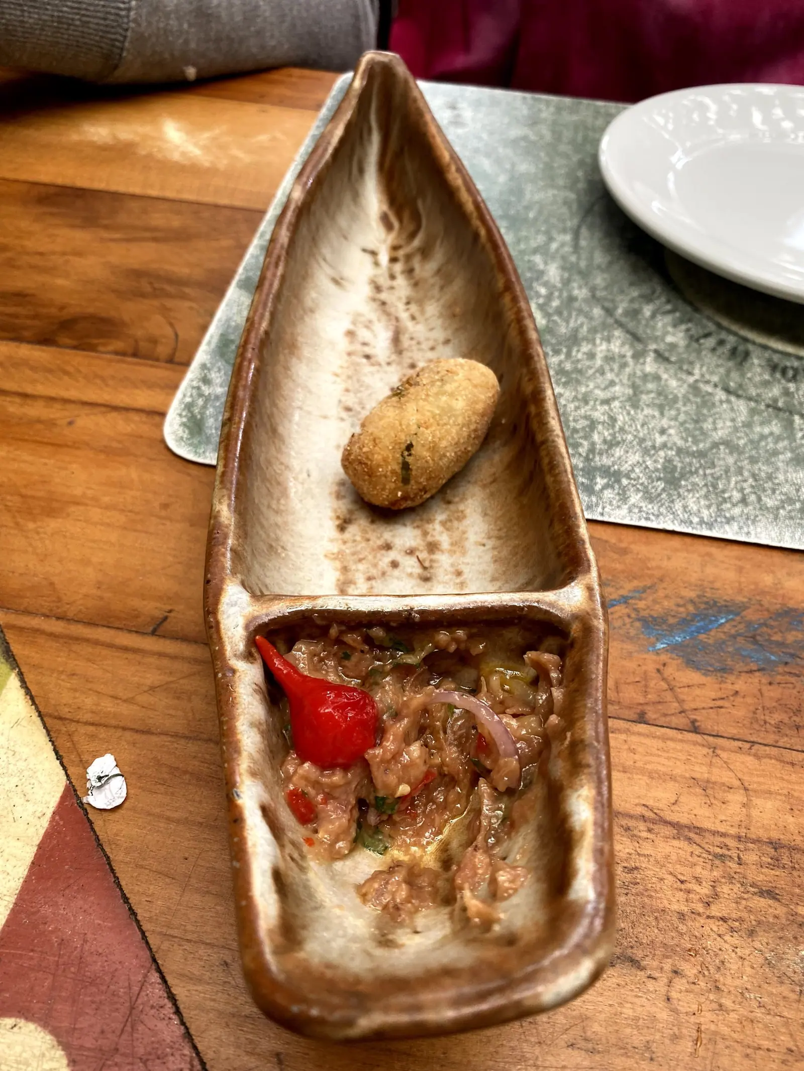 Bolinho e vinagrete servidos em prato de cerâmica em forma de canoa no Taioba