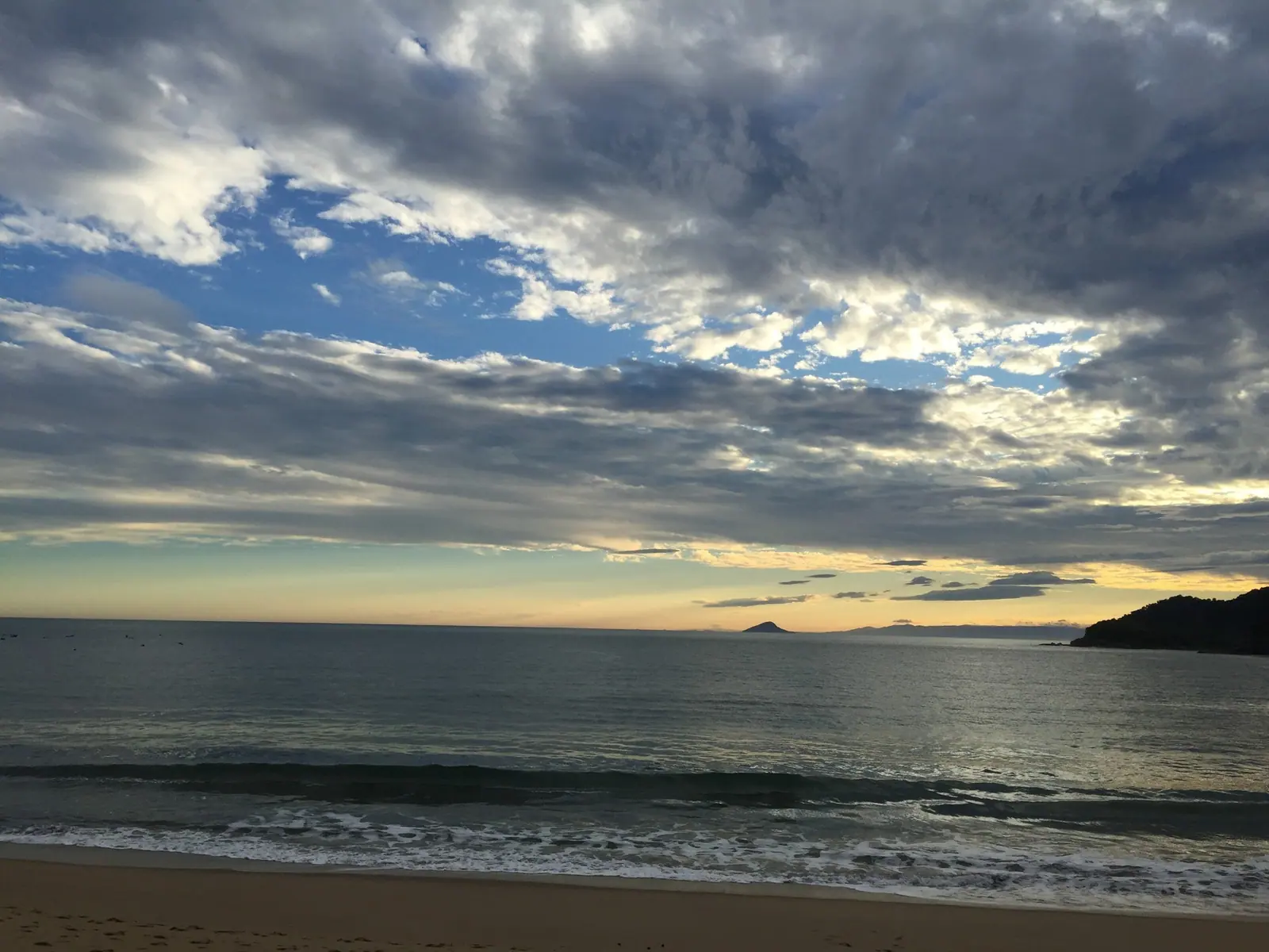 Céu nublado e ondas leves em Toque-Toque Grande, com ilhas no horizonte