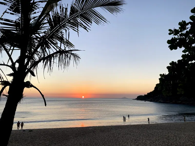 Silhueta de coqueiro e pôr do sol na praia de Toque-Toque Grande, com pessoas na beira do mar