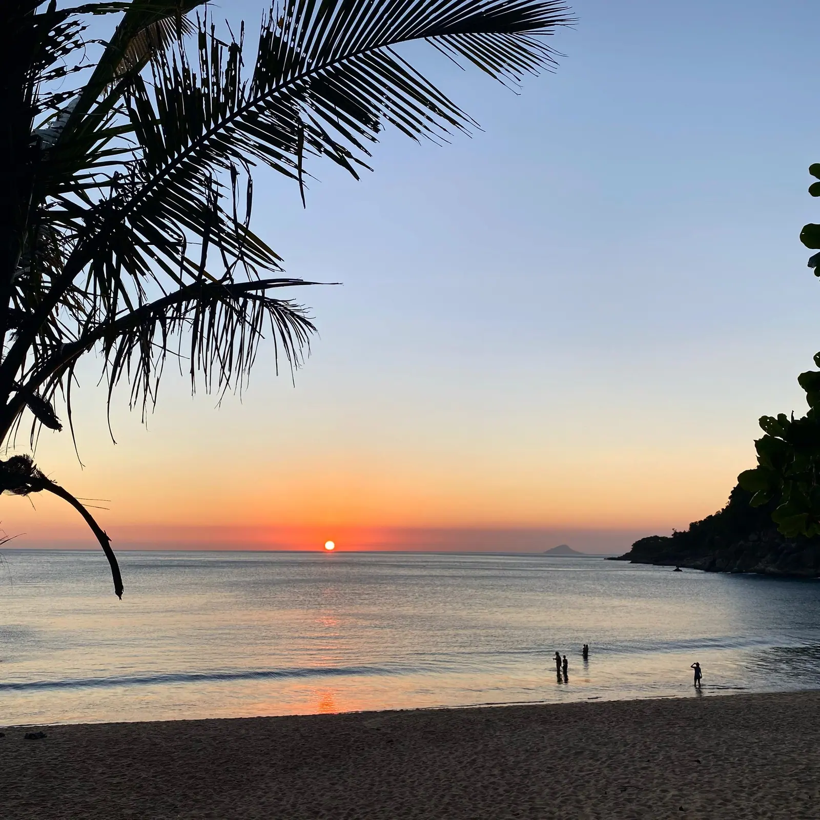 Silhueta de coqueiro e sol no horizonte de Toque-Toque Grande, com banhistas na beira