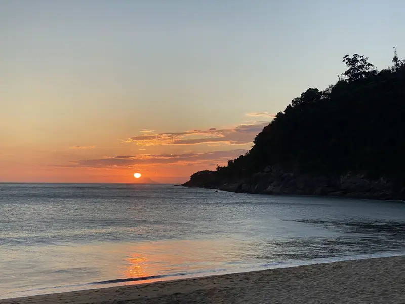 Sol baixo ao lado do costão de mata de Toque-Toque Grande, refletido no mar
