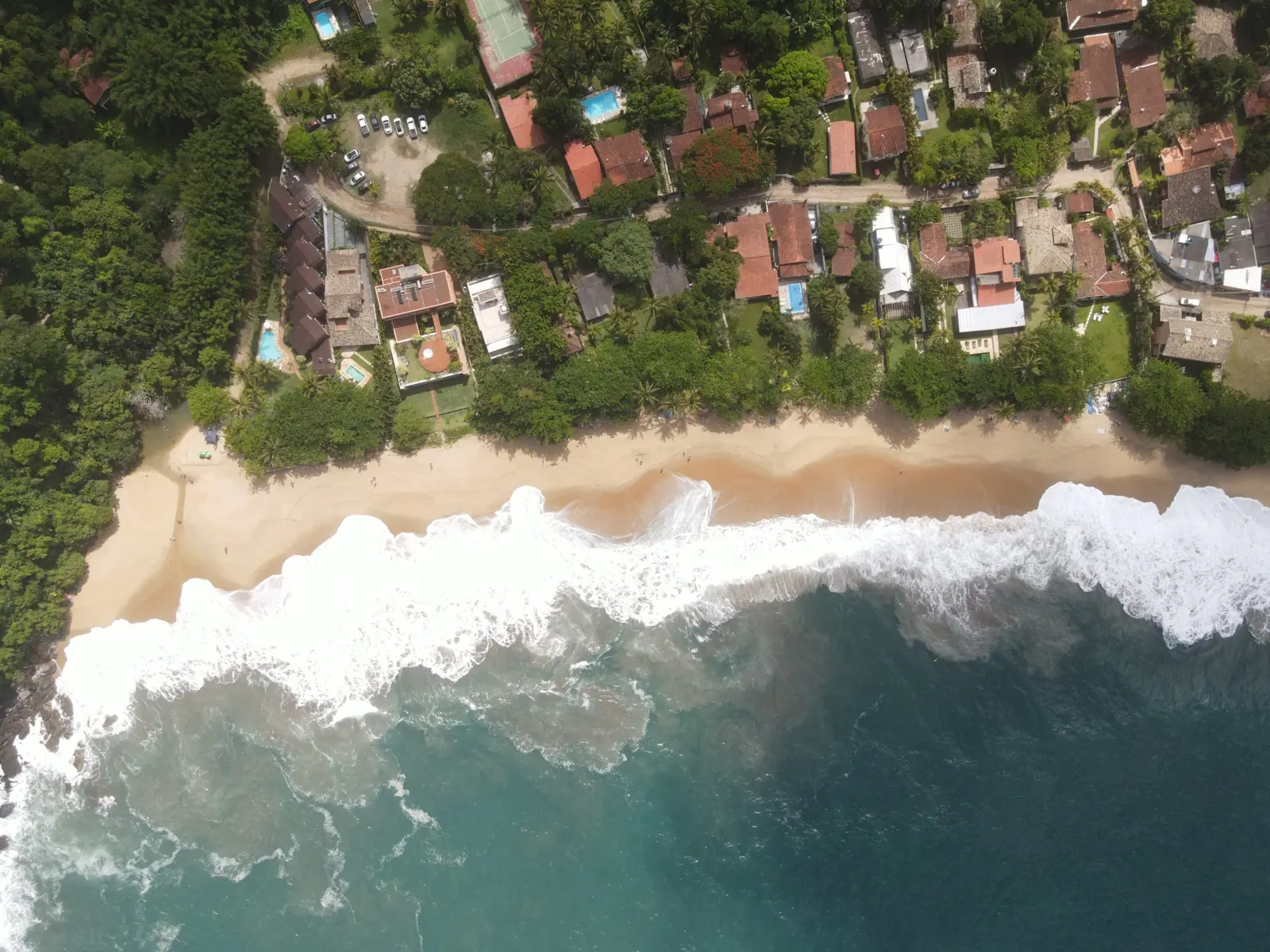 Vista de cima da faixa de areia de Toque-Toque Grande com ondas e as casas atrás da vegetação