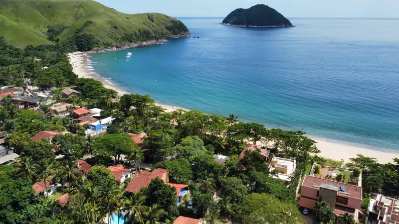 Vista de drone da vila de Toque-Toque Grande, com casas entre coqueiros, a praia em curva e a ilha em frente