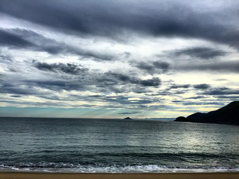 Fim de tarde nublado na praia de Toque-Toque Grande, com o costão à direita e ilhas no horizonte