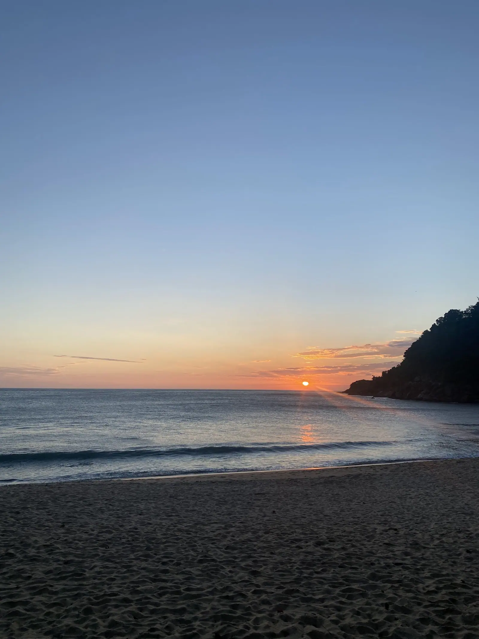 Praia de Toque-Toque Grande ao entardecer, com o sol junto ao costão