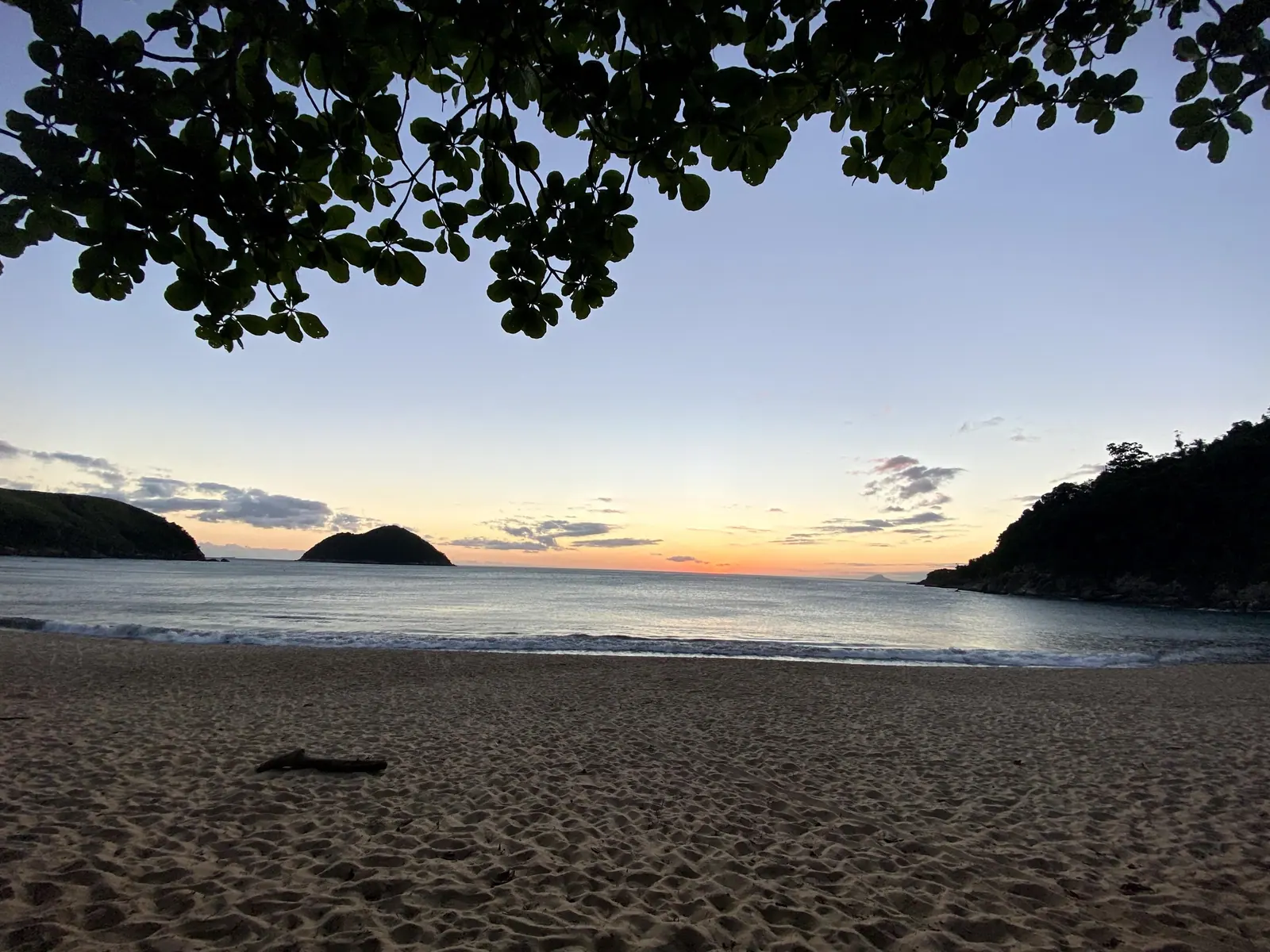 Praia de Toque-Toque Grande vazia ao entardecer, emoldurada por árvores