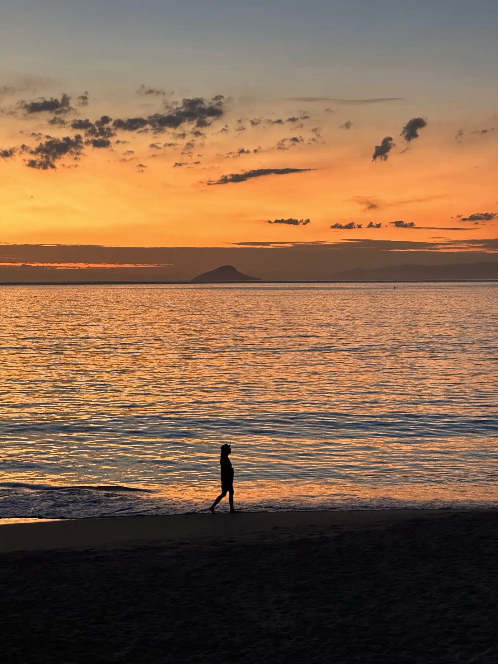 Pessoa em silhueta caminhando na beira do mar de Toque-Toque Grande ao entardecer