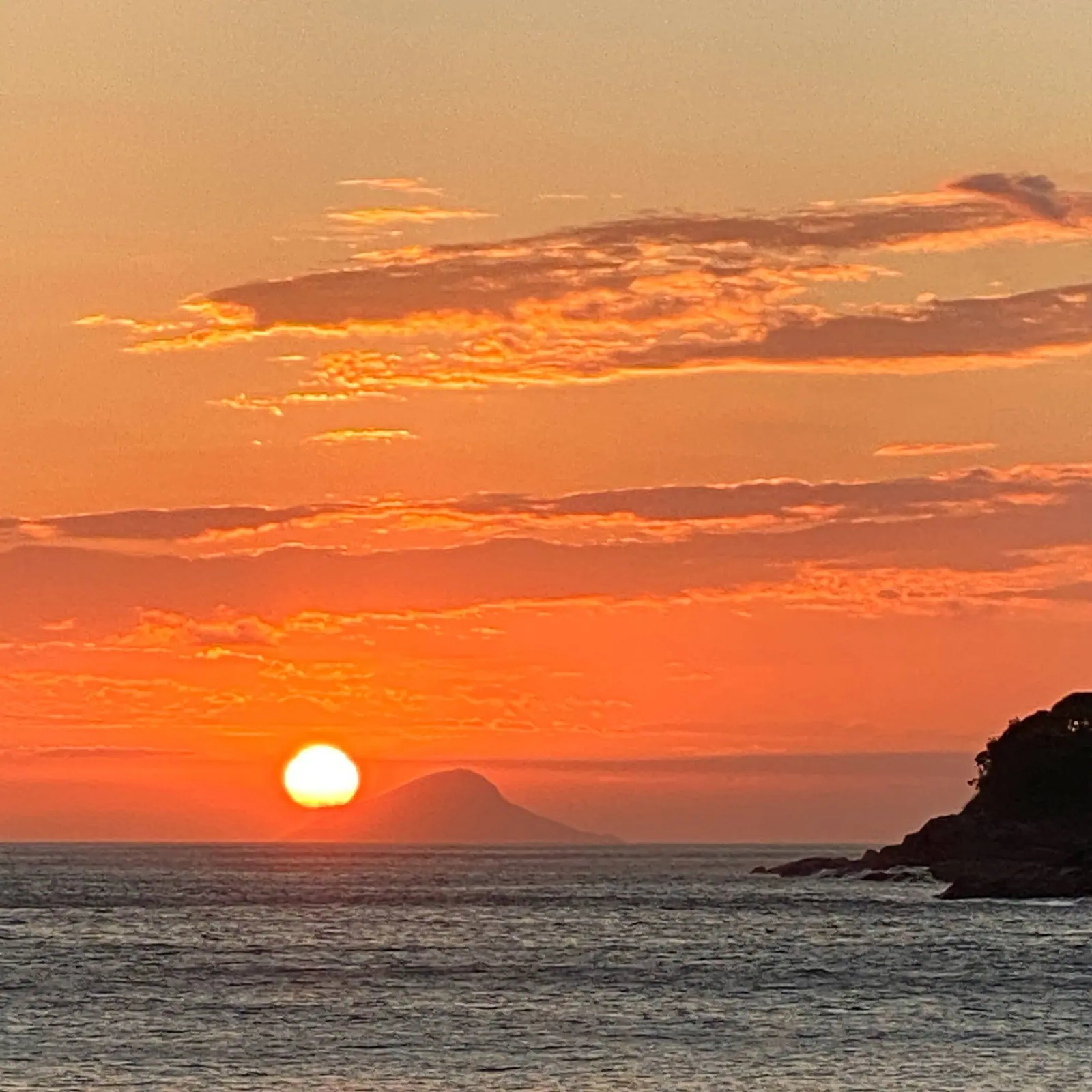 Sol se pondo ao lado de uma ilha em forma de cone, visto da praia de Toque-Toque Grande
