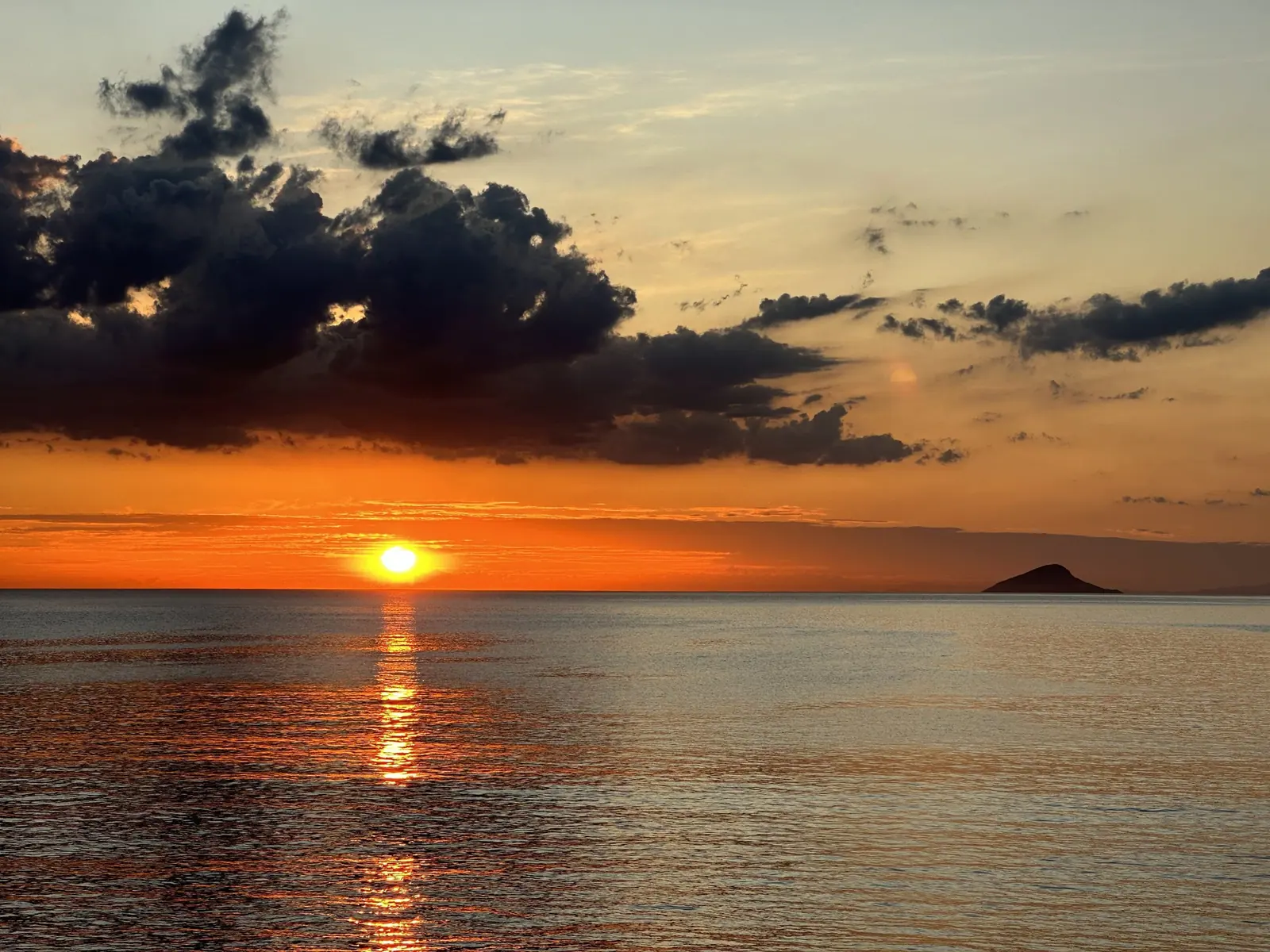 Sol tocando o horizonte em Toque-Toque Grande, com reflexo no mar e uma ilha à direita