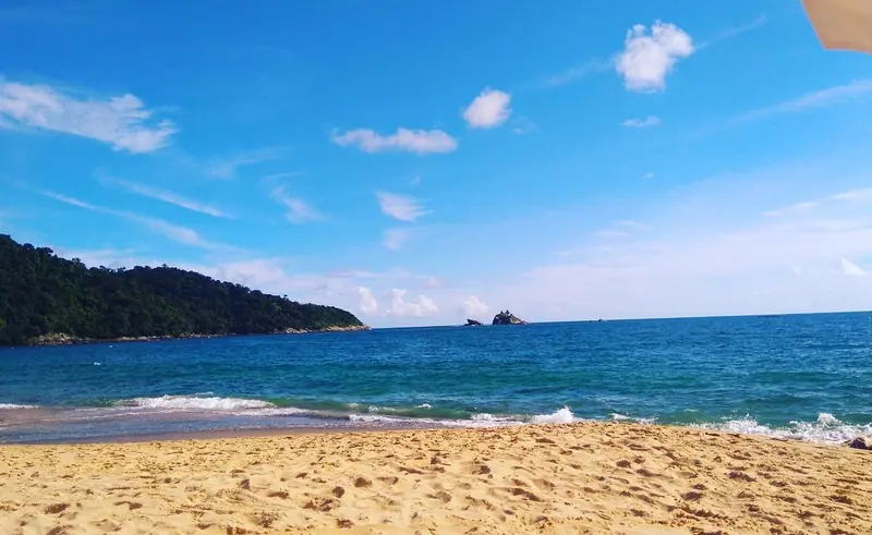 Areia dourada e mar azul em Toque-Toque Pequeno, com o morro e as ilhas ao fundo