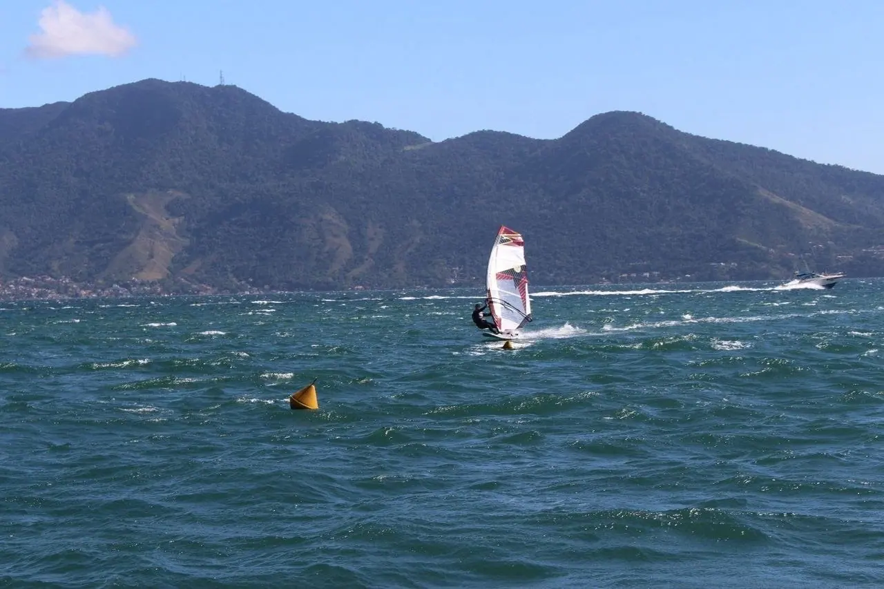 Windsurfista com vento no canal, ao lado de uma boia de regata